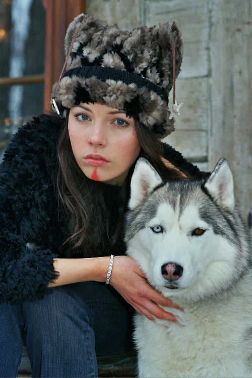 Woman wearing a sheared beaver fur hat and coat sitting next to a husky dog.
